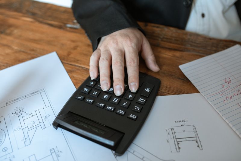 A hand working a calculator on top of printed plans